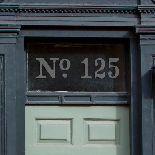 an etch effect custom house door number sticker stuck on to a window above a pale green front door.