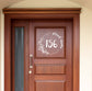 A house door number and street name with floral decorations vinyl decal sticker stuck on to the window above a brown door.